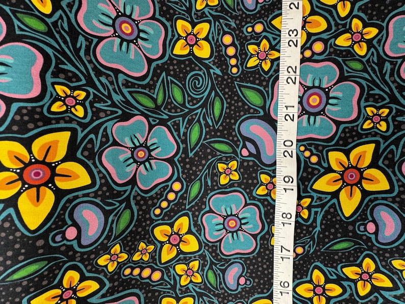 May include: A fabric with a floral pattern featuring large turquoise, yellow, and pink flowers on a black background. Green leaves and small yellow flowers are also present. A ruler shows the fabric's dimensions.