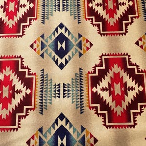Peut inclure: Gros plan sur un tissu beige avec un motif géométrique répétitif. Le motif présente des formes de losanges et rectangulaires en rouge, bordeaux, bleu et jaune, créant une esthétique sud-ouest ou amérindienne.