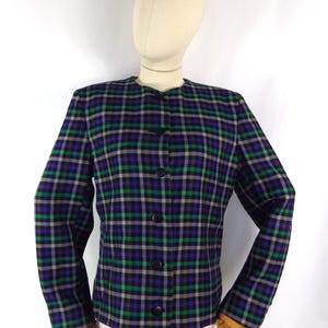 May include: A long-sleeved jacket featuring a plaid pattern in shades of purple, green, black, and white. The jacket has a round neckline, a straight hem, and a front closure with five round black buttons arranged in a vertical line down the centre.