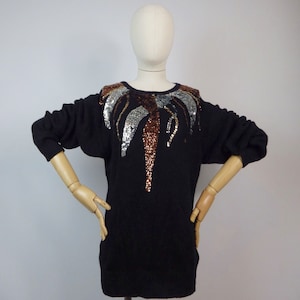 Può includere: Maglione nero con un design a forma di palma in paillettes argento, oro e rame.