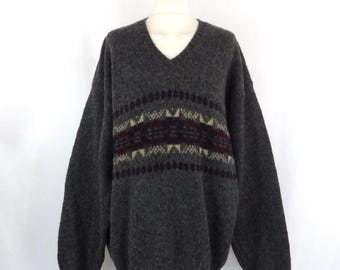 May include: A grey v-neck jumper with a colourful geometric pattern around the chest.