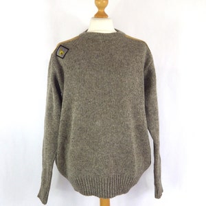 Può includere: Un maglione di lana marrone con una toppa beige sulla spalla. La toppa ha un emblema giallo e bianco.