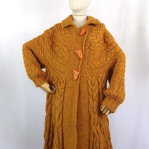 Könnte beinhalten: Ein langer, senfgelber Strickcardigan mit Schalkragen und Holzknöpfen.