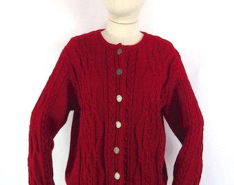 May include: A red cable-knit cardigan sweater with a round neckline and long sleeves. The sweater has a button-up front with silver-colored buttons. The garment is displayed on a mannequin.