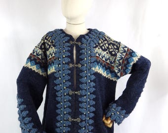 May include: A blue knitted cardigan with a white and brown geometric pattern. The cardigan has a crocheted trim and silver buttons.
