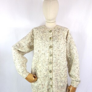 May include: A cream-colored cardigan with a speckled pattern and a button-up front. The cardigan has two patch pockets and long sleeves.