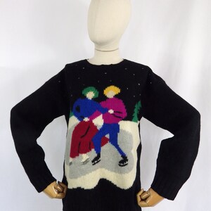 May include: Black knitted sweater with a colourful graphic of two people ice skating on a white background. The graphic is surrounded by a black border.