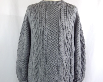 May include: A gray cable knit sweater with a crew neck. The sweater has a textured pattern and is made of a soft, warm material.