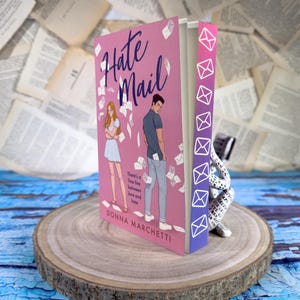 May include: A pink paperback book titled "Hate Mail" by Donna Marchetti. The cover features a couple standing back to back with envelopes flying around them. The text "There's a fine line between love and hate" is printed on the cover.