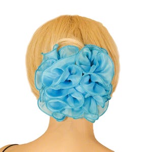 May include: A bright blue hair accessory featuring multiple layers of sheer, ruffled fabric arranged in a circular, flower-like shape. The edges of the fabric are finished with a matching blue stitched trim, creating a voluminous, textured appearance.