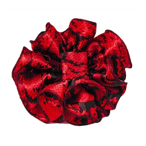 May include: A ruffled scrunchie in a vibrant red color with a black snakeskin pattern. The scrunchie is made of a shiny fabric and has a gathered design, creating a voluminous look. The accessory is suitable for various hairstyles.