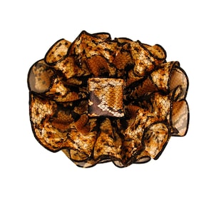 May include: A scrunchie with a snakeskin pattern in shades of brown and black. The scrunchie is gathered and ruffled, with a square accent piece in the center. The fabric has a shiny, silky appearance.