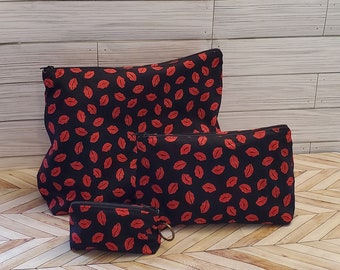 May include: Three black zippered pouches with a red lips print. The pouches are different sizes and are arranged from largest to smallest.