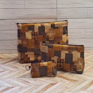 May include: Three zippered pouches with a patchwork design featuring a cross and inspirational text. The text includes "Great Strength Comes From Faith in God" and "Courageous Your God".