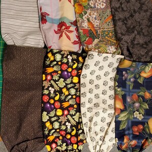 May include: Nine reusable grocery bags made of fabric with various patterns. The patterns include stripes, flowers, vegetables, and geometric designs. The bags are all folded and laid out on a green surface.