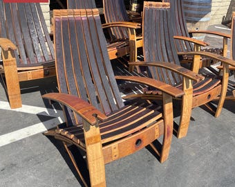 May include: A set of outdoor chairs constructed from repurposed oak wine barrels, featuring curved staves with dark stained interiors and natural wood exteriors. Each chair has wide armrests, a tall slatted back, and a circular bung hole detail.