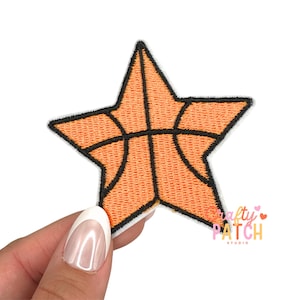 May include: An orange star-shaped patch with a basketball design. The patch has a black outline and the text "Crafty Patch Studio" in pink and white. The patch is held by a person.