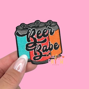 May include: Embroidered patch featuring three beer cans in teal, red, and orange. The patch has the words "Beer Babe" in a cursive font. The patch is a fun accessory for jackets, bags, or other items.