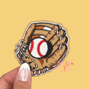 May include: Embroidered patch featuring a baseball glove and ball. The glove is tan with brown accents and stitching, and the baseball is white with red stitching. The patch has a cream-colored border and is set against a yellow background.