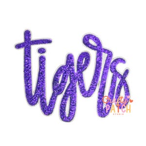 May include: A purple sequined patch with the word "Tigers" in a cursive font. The letters are outlined in white and the patch has a white background. The patch is likely for apparel or accessories.