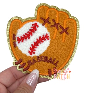 May include: A baseball glove patch with a baseball. The patch is orange with a gold glitter border. The baseball is white with red stitching. The word "BASEBALL" is stitched in brown.