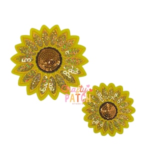 May include: Two yellow sunflower patches with brown centers and gold sequins. The petals are yellow with a scalloped edge. The center of each flower is brown with gold sequins. The patches are on a white background.