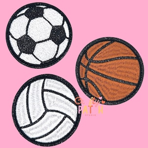 May include: Three embroidered patches featuring sports balls: a soccer ball with black and white pentagons, a brown basketball with black lines, and a white volleyball with black lines. Each patch has a black glittery border.