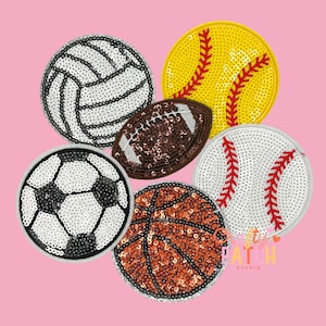 May include: A collection of sequined sports ball patches, including a volleyball, softball, baseball, basketball, and football, against a pink background. Each patch is round or oval, with detailed stitching and vibrant colors.