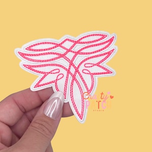 May include: A white and pink embroidered patch with a stylized floral design. The patch features a white background with a pink, interwoven design and pink stitching around the edges. The patch is held against a yellow background.