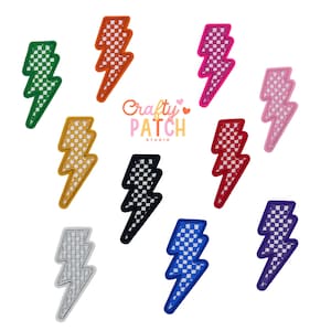 May include: A collection of embroidered lightning bolt patches in various colors, including green, orange, pink, red, yellow, black, silver, blue, and purple. Each patch features a checkered pattern and a contrasting border. The "Crafty Patch Studio" logo is visible.