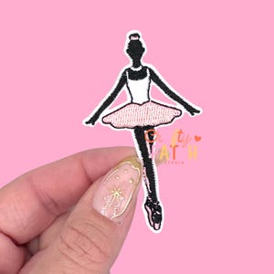 May include: Embroidered patch featuring a ballerina in a black silhouette with a white leotard and a pink tutu. The patch has a white border and is set against a pink background. The text "Pretty Patch Studio" is visible.