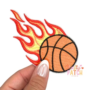 May include: Embroidered patch featuring a basketball engulfed in flames. The basketball is orange with black lines, and the flames are red, orange, and yellow. The patch is on a white background. The text "Crafty Patch Studio" is visible.