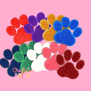 May include: A collection of colorful, textured paw print patches in various colors, including red, purple, gold, blue, green, white, pink, and burgundy. The patches are arranged on a pink background. The text "Crafty Patch Studio" is visible.