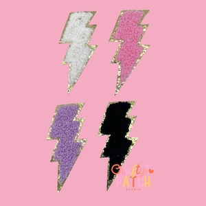May include: Four embroidered lightning bolt patches in white, pink, purple, and black. Each bolt has a gold glitter border and a textured, fuzzy center. The background is a solid light pink.