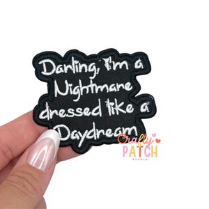 May include: Black embroidered patch with white text that reads "Darling, I'm a Nightmare dressed like a Daydream." The patch has a black border and is held by a hand. The patch is from Crafty Patch Studio.