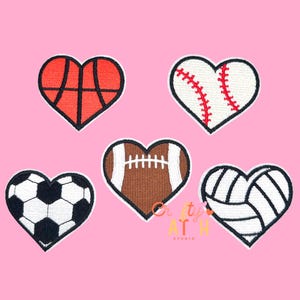 May include: Five heart-shaped patches featuring sports themes. Includes a basketball, baseball, football, soccer ball, and volleyball design. Each patch has a black outline and is set against a pink background. The patches are embroidered.