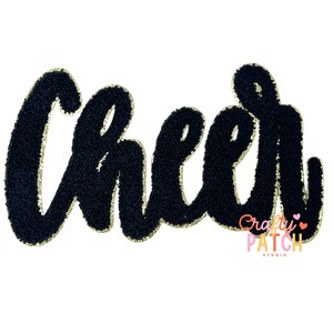 May include: A black chenille patch with the word "Cheer" in a cursive font, outlined in gold. The patch has a gold border and a logo for Crafty Patch Studio.