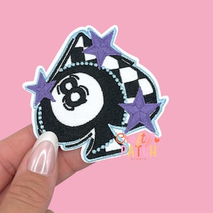May include: Embroidered patch featuring a black and white eight ball design with a checkered flag and three purple stars. The patch has a light blue border and the number 8 is prominently displayed.