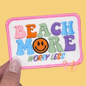 May include: Embroidered patch with the words "BEACH MORE WORRY LESS" in colorful bubble letters. The patch features a smiling face and a pink border. The patch is rectangular.