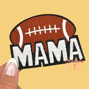 May include: A brown and white football patch with the word "MAMA" in white block letters. The patch has a black border and is on a yellow background. The football is stitched with white laces.