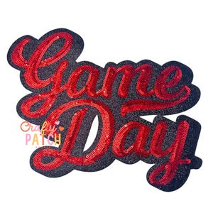 May include: A sequined patch with the words "Game Day" in red script lettering. The letters are filled with red sequins and outlined with a black glittery border. The patch is designed for apparel and crafts.