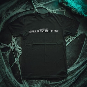 Puede incluir: Camiseta negra con texto blanco que dice "Dirigida por Guillermo del Toro".