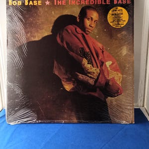 May include: A vinyl record album cover titled The Incredible Base by Rob Base. The cover features a portrait of a person wearing a red jacket against a dark background. A yellow circular sticker on the top right lists 10 new hits including Turn It Out.