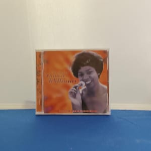 Könnte beinhalten: Eine quadratische Musik-CD-Hülle mit einem schwarz-weißen Porträt von Deniece Williams auf orangefarbenem Hintergrund. Der Text lautet The Best of Deniece Williams und Gonna Take a Miracle. Die Hülle besteht aus klarem Kunststoff mit sichtbarem Rücken.