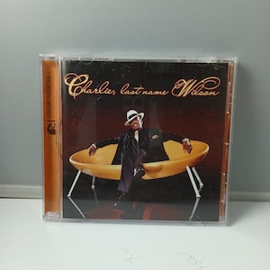 May include: CD case featuring the album "Charlie, last name Wilson." The cover art shows a man in a suit and hat seated on a yellow sofa. The album title is in gold script.