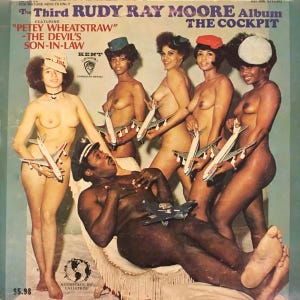 May include: A vintage record album cover featuring a black man and four women, all nude, holding toy airplanes. The album title is "The Third Rudy Ray Moore Album" and the subtitle is "The Cockpit". The album features "Petey Wheatstraw - The Devil's Son-In-Law".