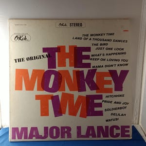 Peut inclure: Une pochette de disque vinyle vintage pour The Monkey Time de Major Lance sur le label Okeh. La couverture blanche présente un grand texte orange et violet superposé indiquant The Monkey Time, avec une liste de titres dont Land of a Thousand Dances.