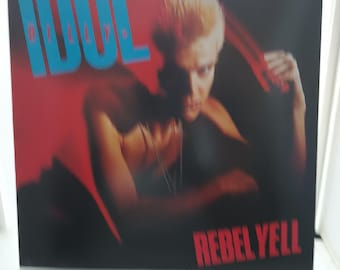 May include: Album cover for Billy Idol's "Rebel Yell." The artwork shows a shirtless person with spiky blonde hair against a red and black backdrop. The word "IDOL" is in large, turquoise letters, and "REBEL YELL" is in red.