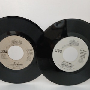 May include: Two black vinyl records with white labels. One label reads "Beat It" by Michael Jackson, the other reads "Off The Wall" by Michael Jackson. Both records are 45 RPM.