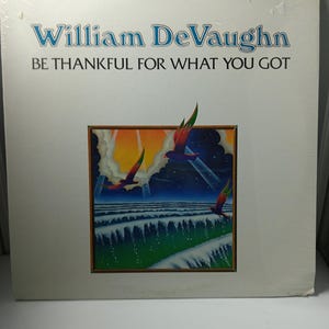 Può includere: Una copertina di un album in vinile con il testo "William DeVaughn" in blu e "BE THANKFUL FOR WHAT YOU GOT" in nero. L'artwork mostra uccelli in volo su un paesaggio stilizzato con tonalità blu e verdi.